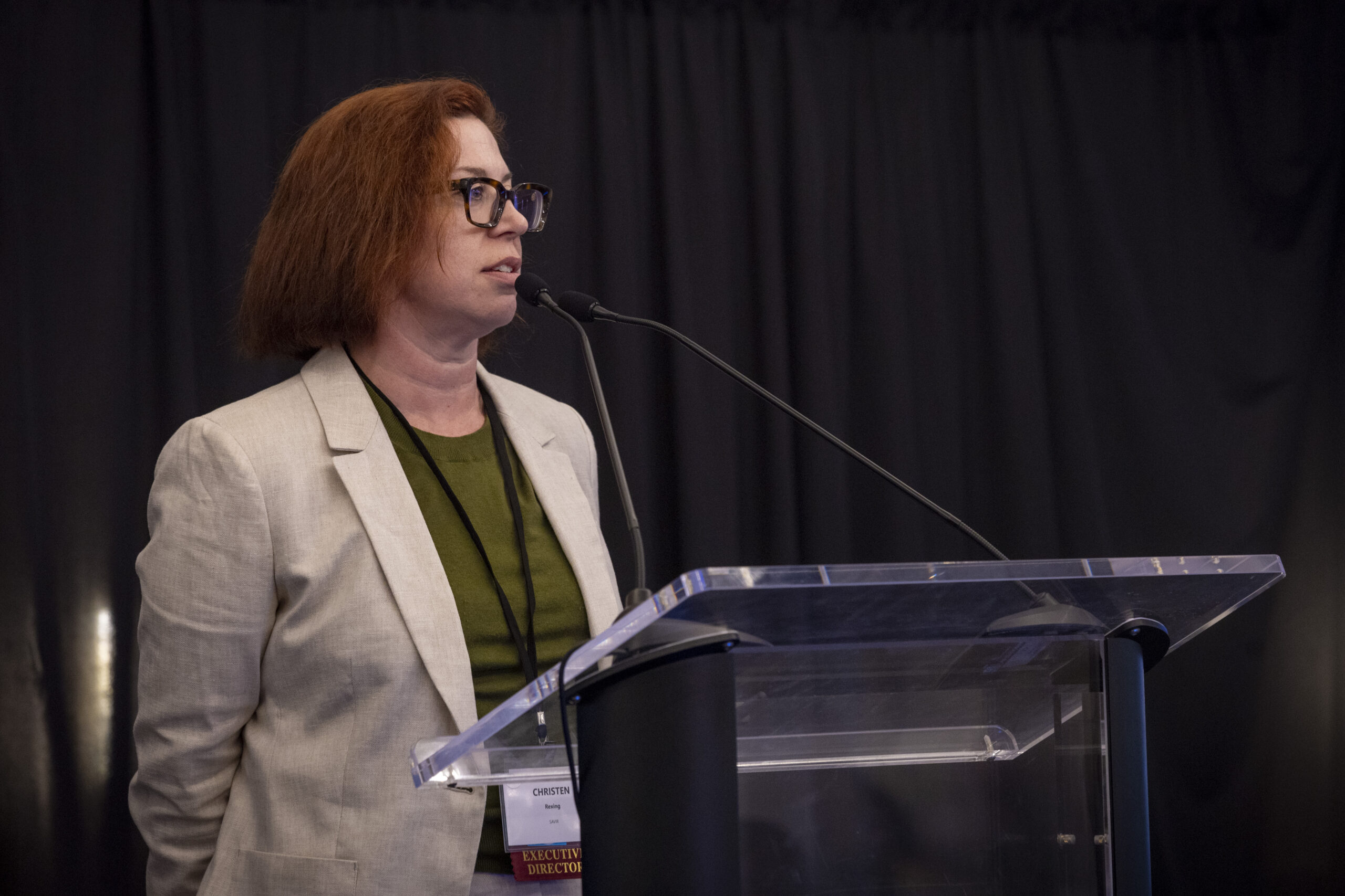 A woman standing at a podium speaking to an audience.