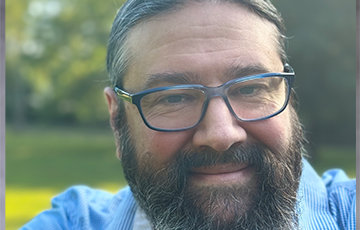 A man with long beard and glasses smiling for the camera.