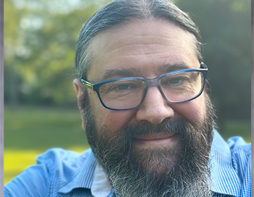 A man with long beard and glasses smiling for the camera.