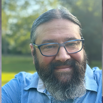 A man with long beard and glasses smiling for the camera.